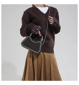 Détail d'un sac à main en cuir marron foncé avec rivets argentés et anse en métal