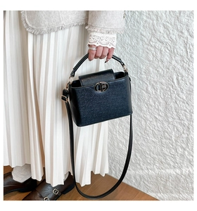 Detail of black bucket bag showing leather texture and golden metal buckle decoration