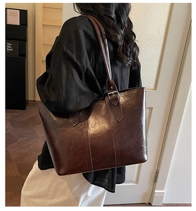 Detail of a large dark brown polished leather tote bag styled on a female model