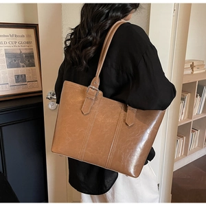 Detail of a large brown leather tote bag showing textured finish and adjustable buckle strap