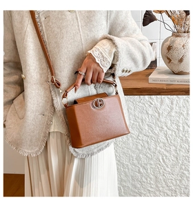 Detail of a brown lychee pattern PU leather bucket bag showing metal logo and texture