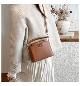Detail of brown leather bucket bag styled with a white tweed jacket and pleated skirt