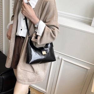 Minimalist black shiny leather hobo bag with gold buckle shown on a model
