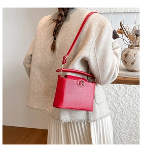 Model showing a red bucket bag with a metal logo in a minimalist French style setting
