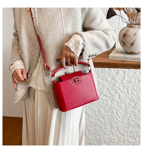 Detail of red textured bucket bag with metal logo, top handle, and thin shoulder strap