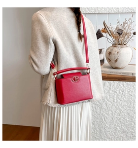 Red leather bucket bag with gold buckle detail worn crossbody by model in home setting