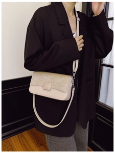 Dettaglio di una borsa a tracolla beige con fibbia quadrata su modella in abito nero