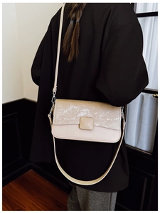Vista posteriore di una modella con borsa a tracolla quadrata color crema con patta strutturata