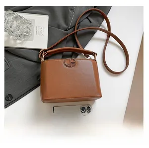 Detailed view of caramel leather bucket bag texture and logo next to a phone for scale