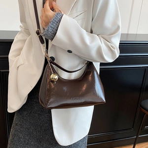 Sac à main en cuir verni marron foncé avec breloque dorée porté par un mannequin en studio