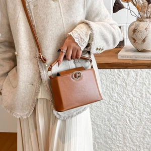 Brown leather bucket bag with top handle and shoulder strap for women in indoor setting