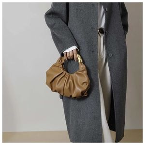 Détail d'un sac nuage plissé marron avec poignée en métal doré sur un manteau
