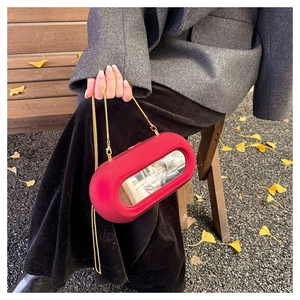 Outdoor shot of a red capsule acrylic bag with mirror detail and gold chain strap