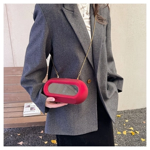 Detail of red acrylic crossbody bag with oval clear window and gold chain strap
