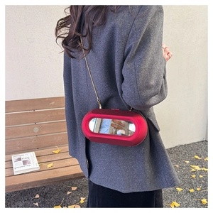 Detail of red acrylic crossbody bag with mirror panel and gold chain on gray blazer