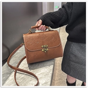 Detail of vintage brown square bag featuring embossed floral patterns and bronze twist lock