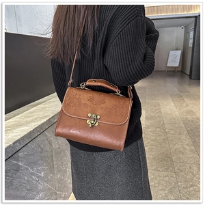Detailed close-up of vintage brown crossbody bag with floral embossed flap and bronze clasp