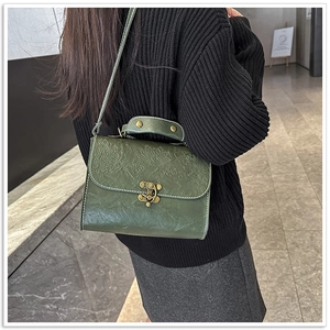 Model wearing a vintage dark green crossbody bag with floral embossing and bronze clasp