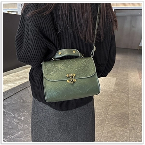 Model wearing a vintage dark green embossed leather handbag with bronze lock detail