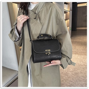 Close-up of black retro crossbody bag with floral embossing and bronze metal lock