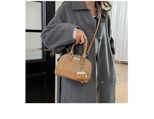 Detail of shell-shaped crossbody bag with woven texture and brown leather patchwork