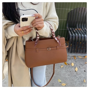 Close-up of brown litchi pattern leather handbag with decorative scarf and long strap