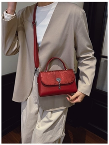 Detail of red leather messenger bag with silk flap and silver key charm on a model