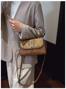 Detail of a brown leather messenger bag with gold textured flap and silver lock pendant