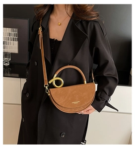 Brown semi-circle leather bag detail with gold metal handle and long strap on black coat