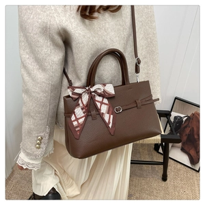 Detail of brown litchi pattern leather tote bag with elegant silk scarf on handle