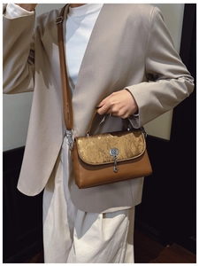 Detail of a brown messenger bag with gold textured flap, silver lock and key charm