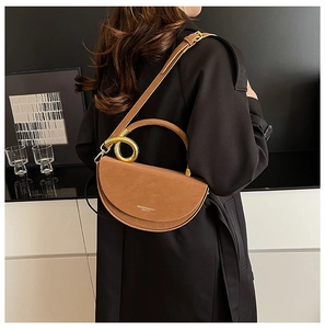 Detail of a brown leather saddle bag with gold circular handle and adjustable shoulder strap