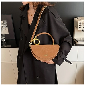 Detail of a brown moon-shaped leather handbag with gold metal ring handle and strap