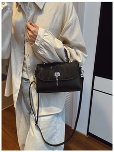 Detail of black leather messenger bag with glitter flap and silver key pendant shown on model