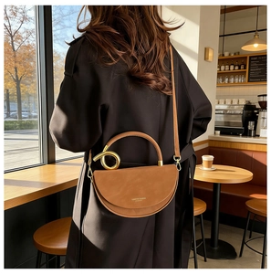 Brown leather half-moon crossbody bag with large round metal handle worn by model