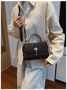 Detail of black messenger bag with vertical texture flap and silver metal lock pendant