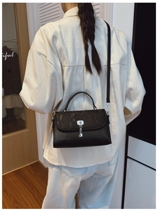 Rear view of model wearing a black messenger bag with vertical ribbing and silver lock