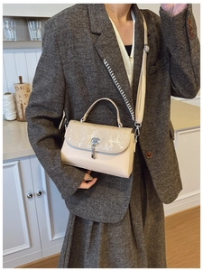 Close-up of beige messenger bag with silver key lock and textured glitter flap