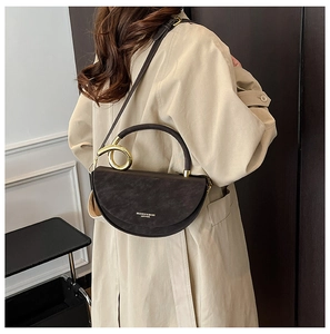 Detail of a dark brown saddle bag with a gold metal ring handle and adjustable strap