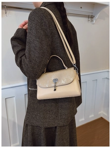 Detail of a beige leather messenger bag with vertical texture and metal lock closure