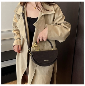 Detail of dark brown leather half-moon bag with gold circular handle and fine strap