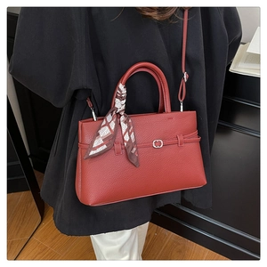 Red lychee grain leather tote bag with decorative silk scarf handle shown on black coat