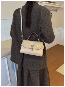 Detail of a beige messenger bag with glitter flap and key lock worn by a model