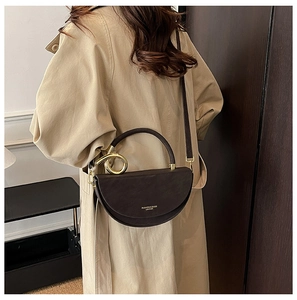 Detail of dark brown leather saddle bag with gold logo and metal ring handle on model