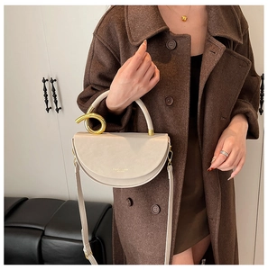 Detail view of cream crescent bag with gold twist ring handle on a brown coat