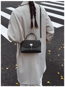Outdoor shot of a black leather messenger bag styled with a beige coat on an autumn street