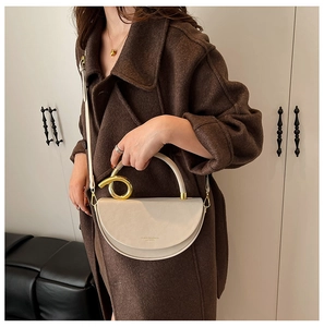 Detail of a beige semicircle leather bag with a unique golden ring handle on a brown coat