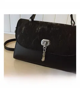 Detail of black corduroy leather messenger bag with silver clasp and key charm