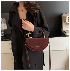 Close-up of luxury burgundy suede saddle bag with unique gold metal ring handle