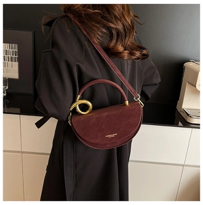 Detail of burgundy suede saddle bag with golden ring handle and leather strap on a model